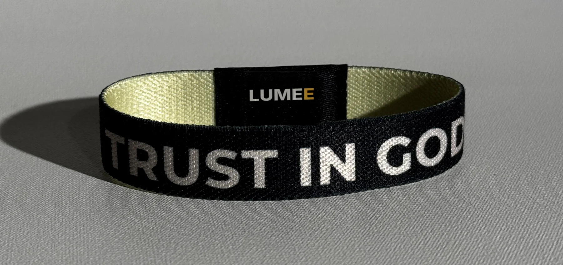 Schwarzes LUMEE-Band mit der Aufschrift Trust in God und dem LUMEE-Patch, innen crème
